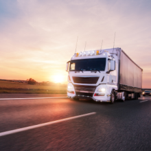 A large white truck on a busy motorway with the sun setting in the distance