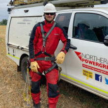 Overhead Linesman, wearing red Personal Protective Equipment, stood next to a white van
