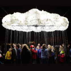 People stood outside in the dark, underneath a large illuminated cloud