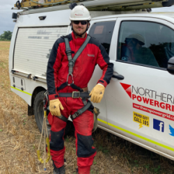 Overhead Linesman, wearing red Personal Protective Equipment, stood next to a white van
